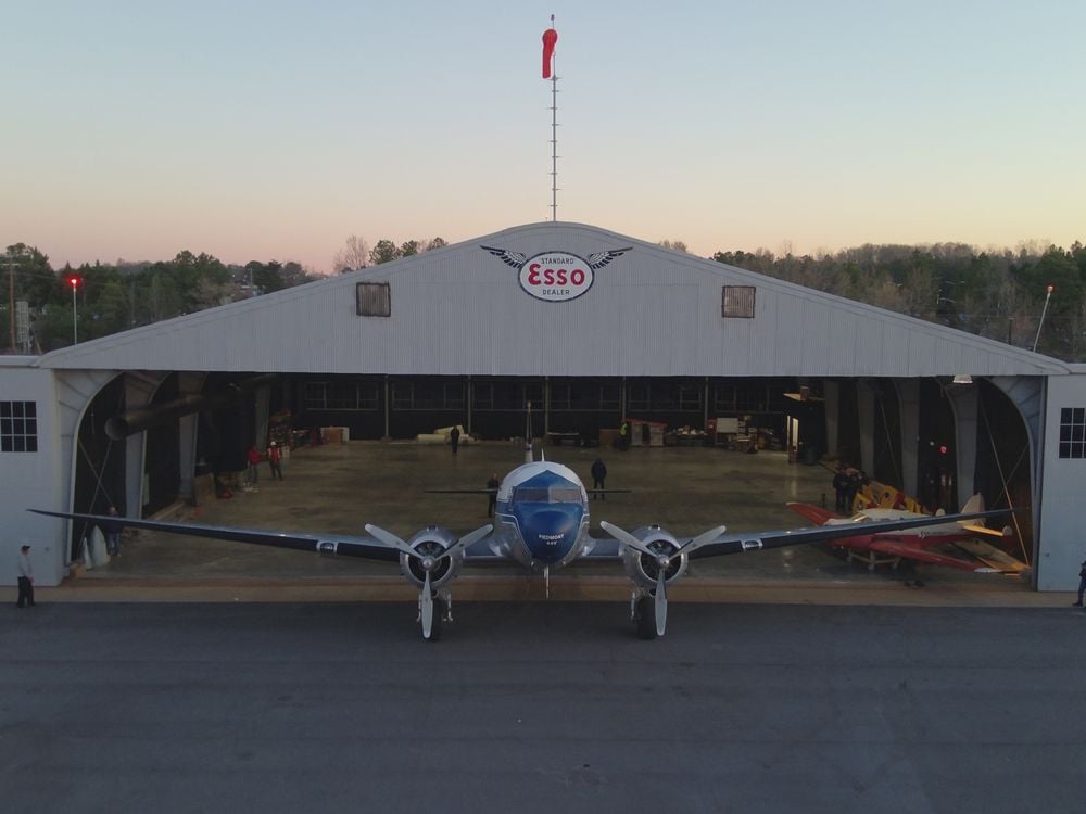 A propellor plane is in front of an open hangar