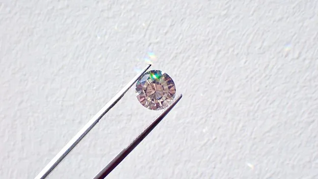 Silver tweezers hold a small diamond against a white background.