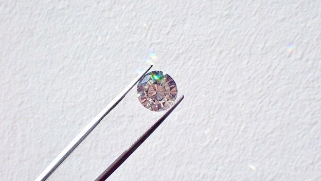 Silver tweezers hold a small diamond against a white background.