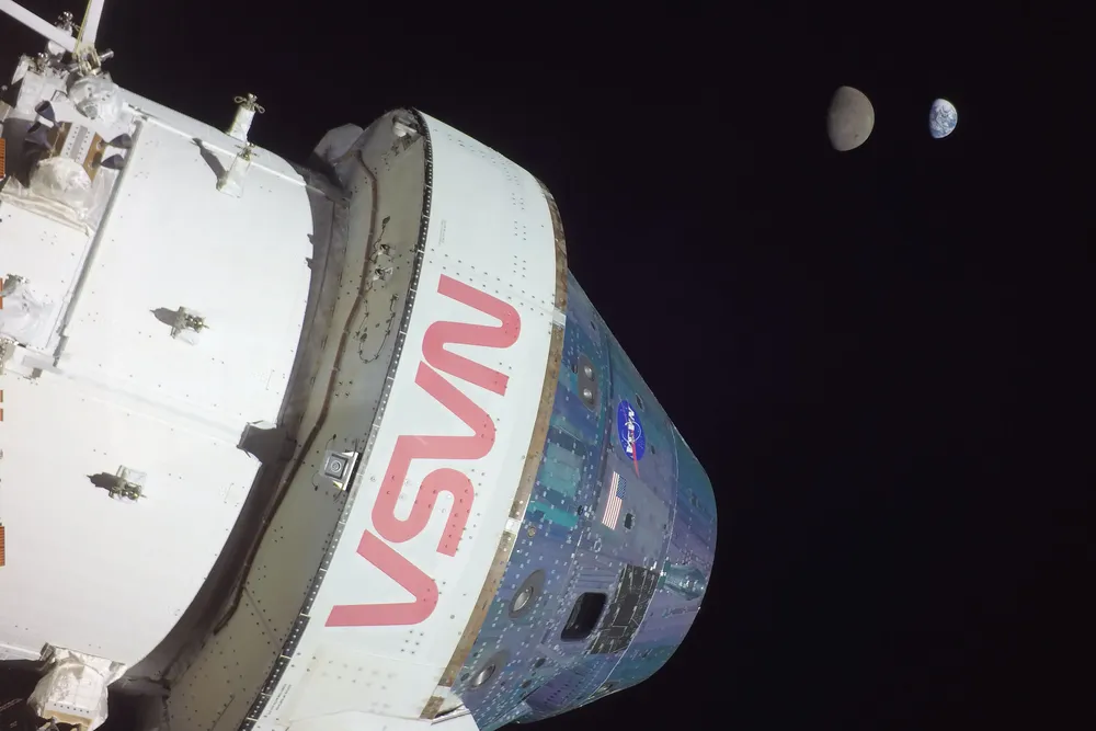 a side view of the Orion capsule from the Artemis 1 mission in space, with the half-lit moon and Earth in the background