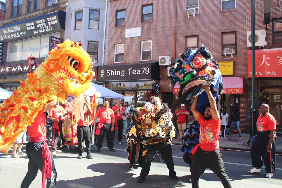 Performers in matching red shirts and black pants perform the Chinese lion dance in the street, hoisting up decorated and glittering lion costumes.