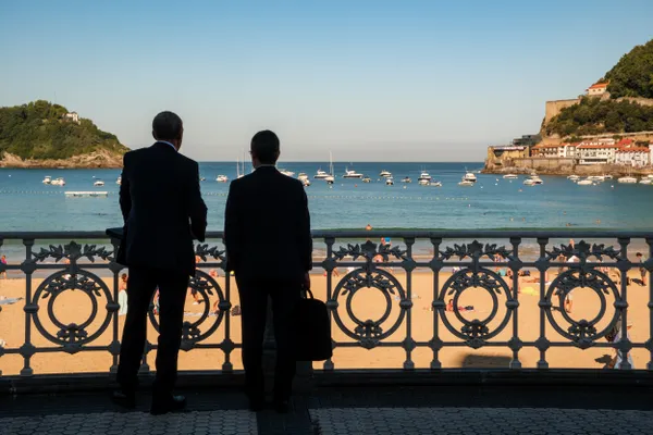 Two men look out at the beach and bay in San Sebastián, Spain. thumbnail