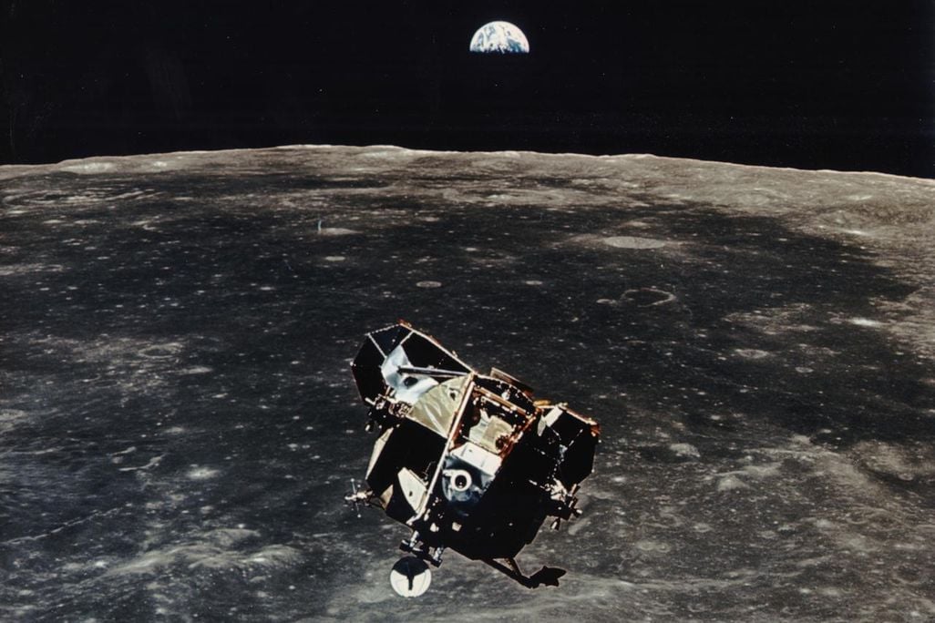 Apollo 11 ascent stage aloft above Earth with the moon rising in the distance