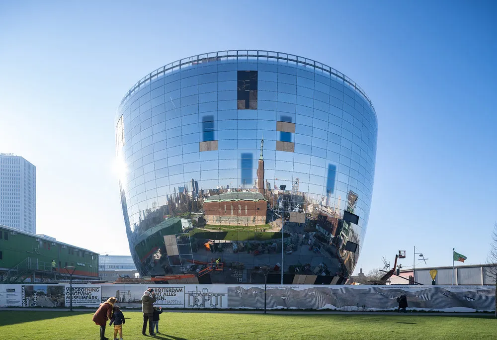A large building shaped like a sphere with a flat top, with mirrors all around the building's surface that reflect the blue sky and white clouds