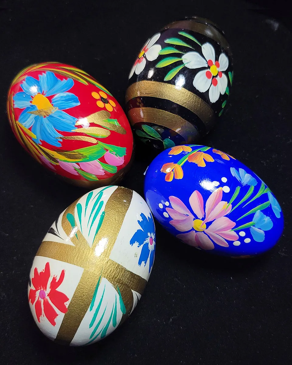 Four intricately painted Easter eggs, each featuring colorful floral designs, displayed against a black background.
