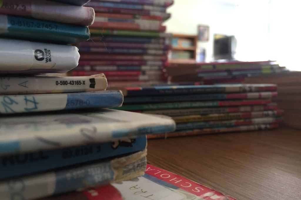 three small stacks of various books sitting on top of brown desk