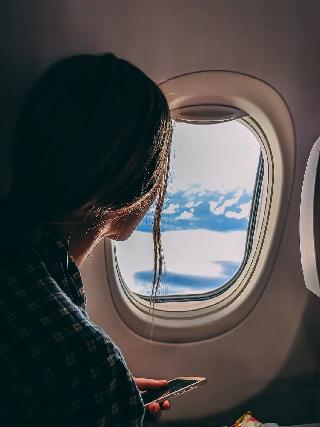 The girl is looking out the window of the plane