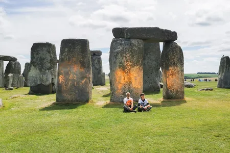 Just Stop Oil protesters&nbsp;Rajan Naidu, 73, and Niamh Lynch, 21, sit in front of Stonehenge after covering the monument in orange powder.