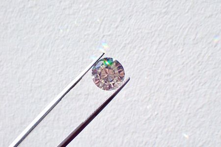 Silver tweezers hold a small diamond against a white background.