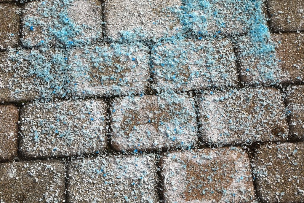 An image of blue road salt covering an icy brick road.