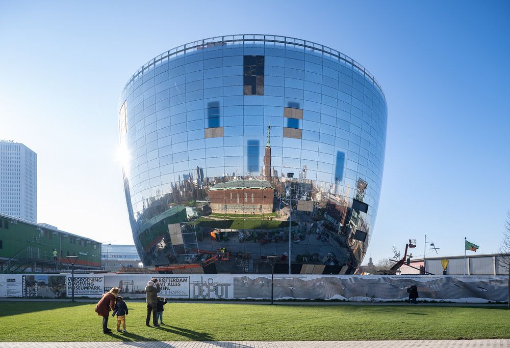 A large building shaped like a sphere with a flat top, with mirrors all around the building's surface that reflect the blue sky and white clouds