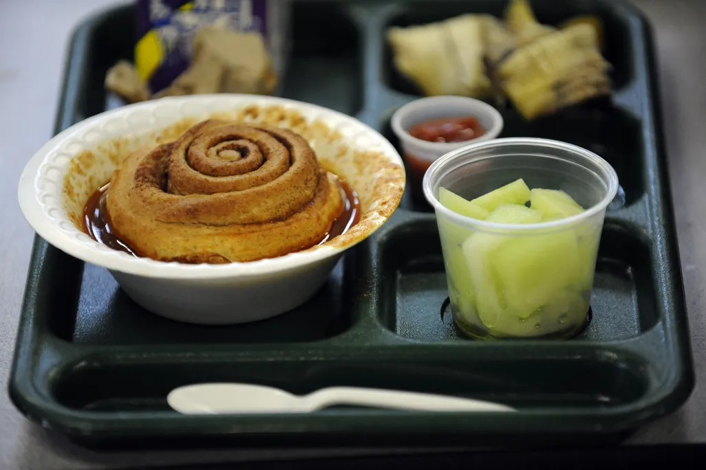 A cup of chili topped with a cinnamon roll on a school lunch tray