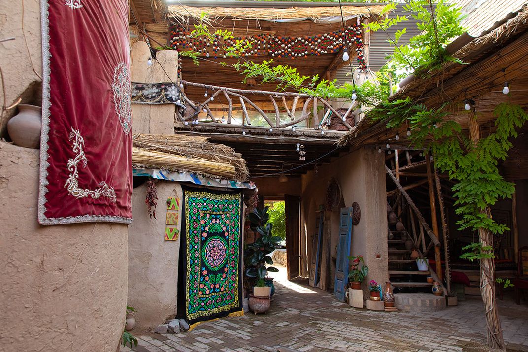 A courtyard among reddish plastered buildings with green vines and hung textiles.