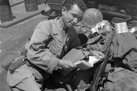 Bound for Morotai Island, Private Bryan Carroll, Memphis, TN, relaxes on the deck of an LST with a book. He leans on a pile of his belongings, which include his helmet and mess kit.