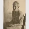 Grandma Moses seated in a chair slightly turned away from the camera holding a book in her lap.
