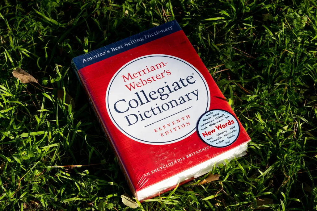 Photo illustration of a Merriam-Webster dictionary in a grass field