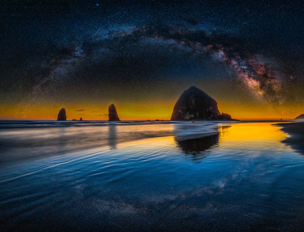While photographing Cannon Beach one summer evening, I witnessed a thick Oregon fog drifting in, obscuring the night sky. And so I added the vast Milky Way panorama I had captured in Death Valley.