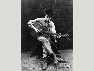 John Cohen photographs a young Bob Dylan playing his guitar and harmonica in New York City in 1962. 