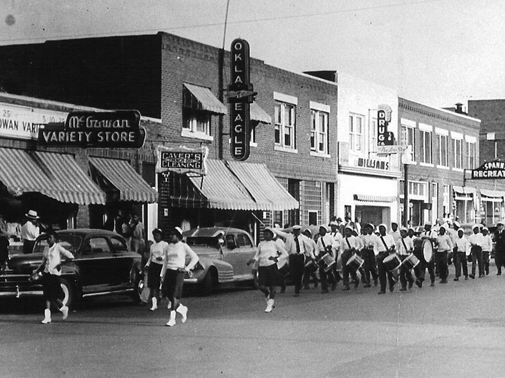 View of an unspecified parade on Greenwood Avenue, Tulsa, Oklahoma, 1930s or 1940s. Among the visible businesses are the offices of the Oklahoma Eagle newspaper at 117 North Greenwood Avenue