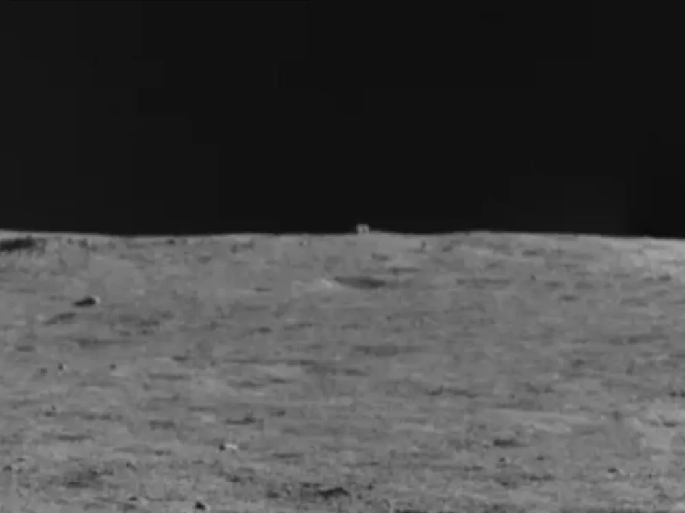 A black and white images of the lunar surface with a small cube-shaped object on the horizon