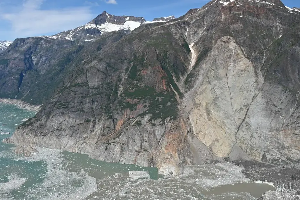Aerial photo of mountain where landslide occurred and foamy water below in the fjord