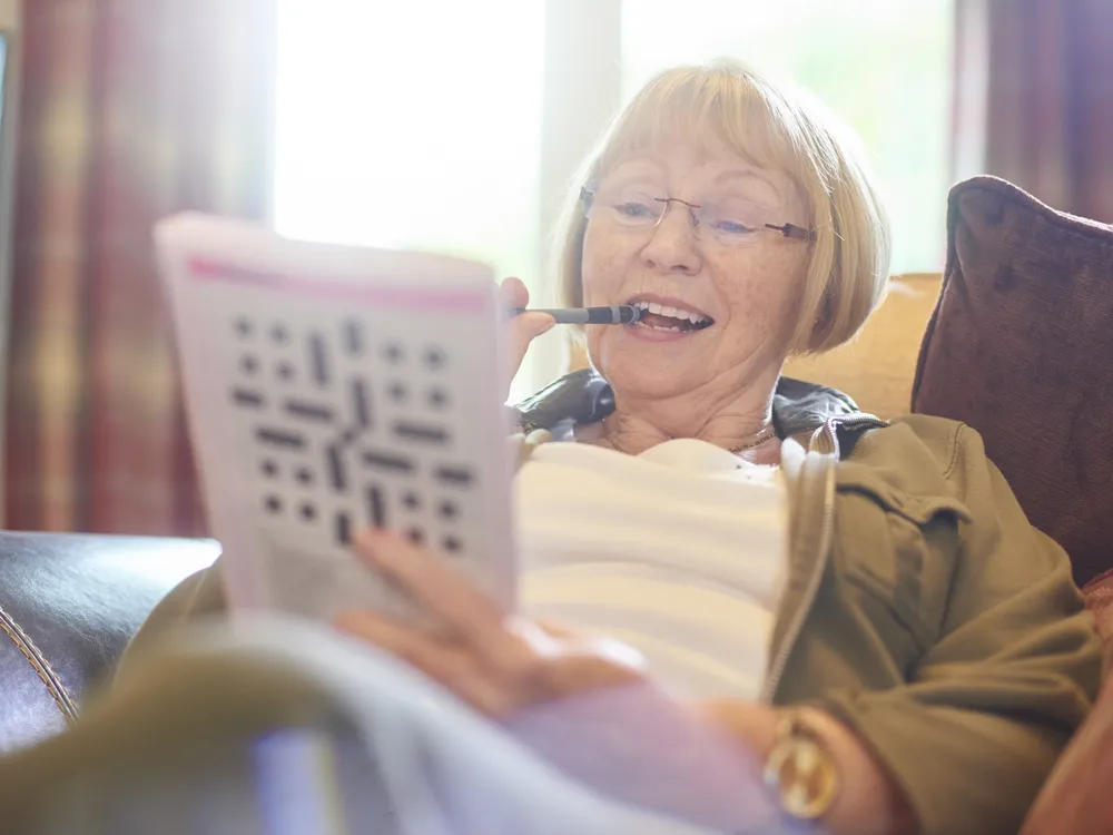 An elderly woman smiles as she does a crossword puzzle