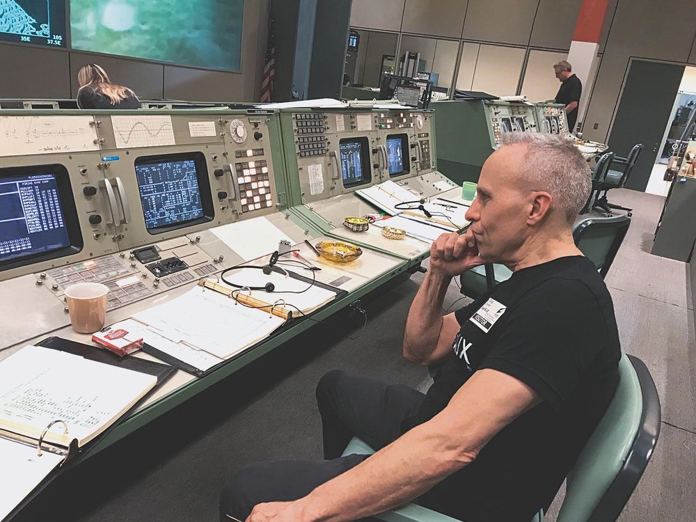 Doug Drexler seated in chair on mission control set