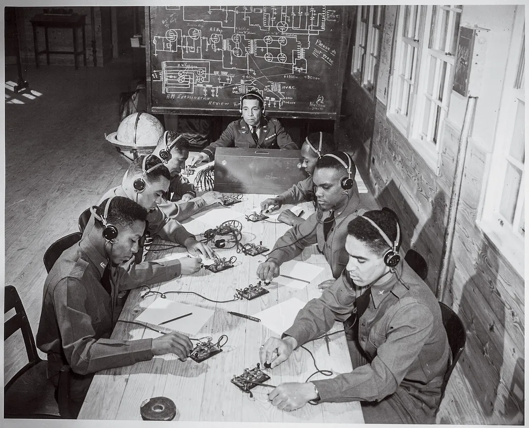 a group of soldiers sit at a table learn the practice of sending out morse code