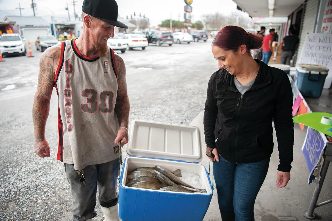 Two people carry a cooler of fish to sell
