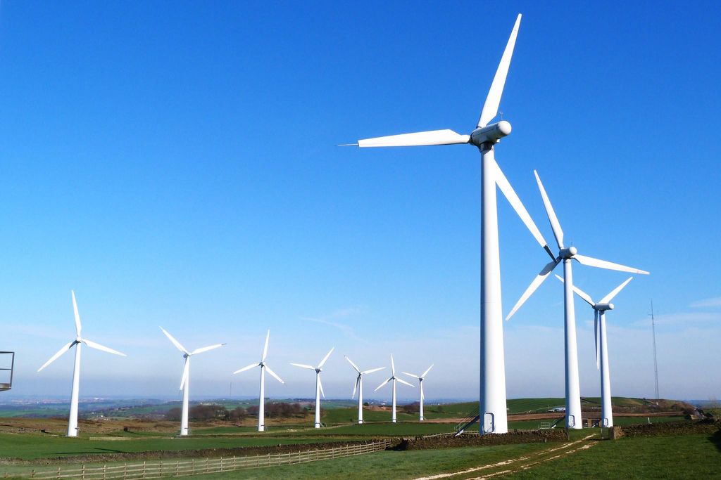 Ten tall, white wind turbines organized in two rows in a grassy field. The sky is bright blue in the background.