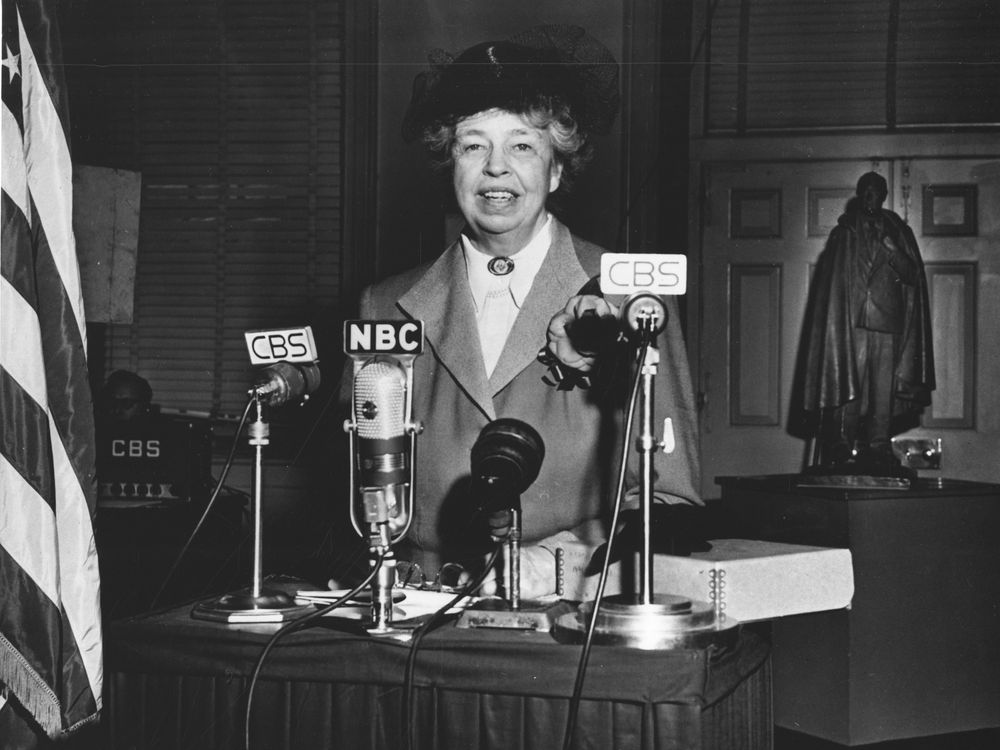 Eleanor Roosevelt standing in front of four microphones labeled as CBS and NBC