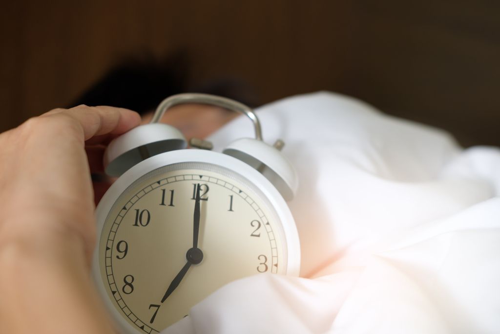 Alarm clock on a bed sheet with a person's hand