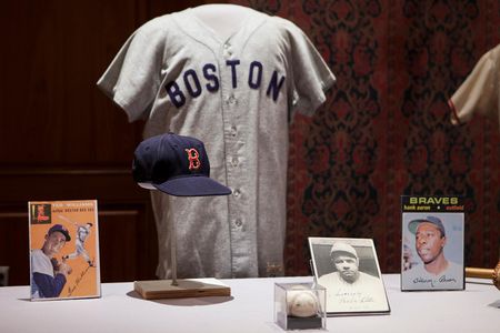 Hat and jersey worn by Ted Williams during his Red Sox reign. The autographed portraits, from left to right, are of Williams, Babe Ruth, and Hank Aaron. Foregrounded is a baseball signed by the members of the "Murderers' Row" 1927 Yankees.