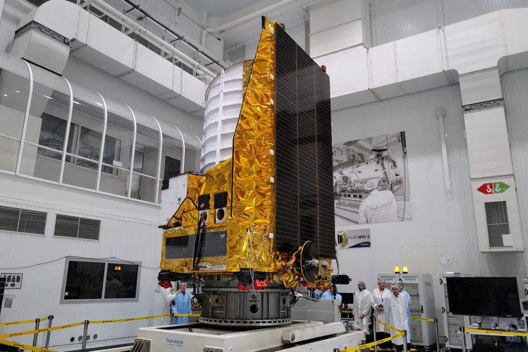 The gold and white Euclid telescope sits in a lab with scientists observing it.
