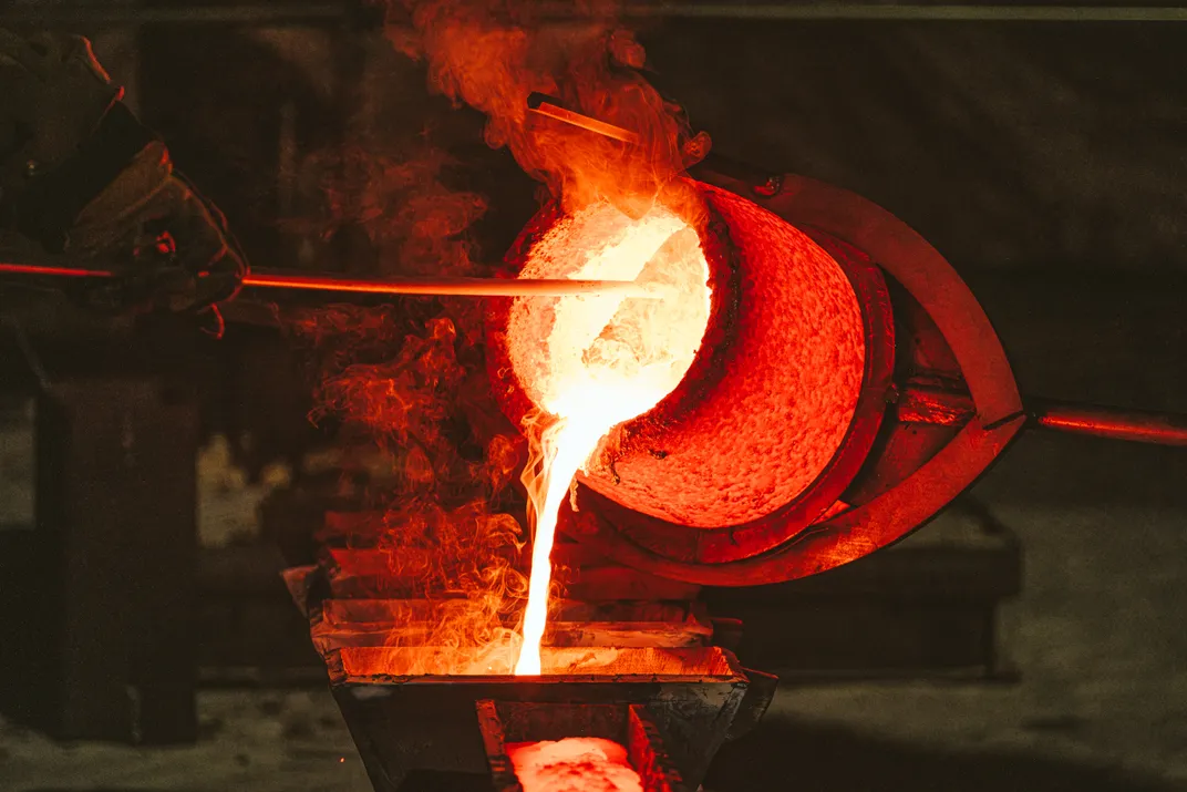 Foundry workers pour molten bronze into mold
