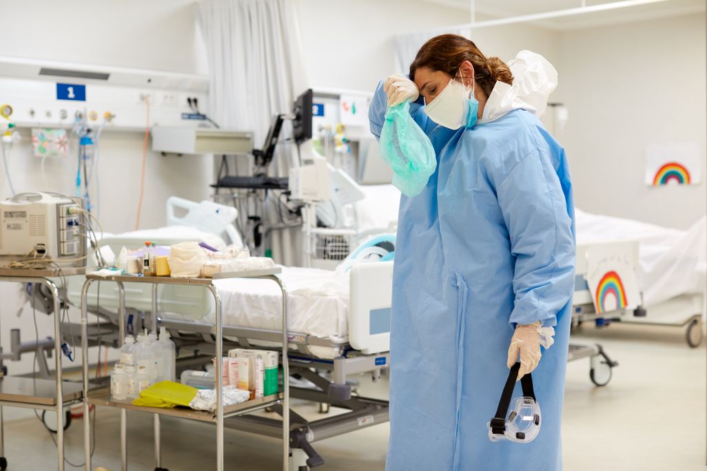 A female ICU doctor with a mask and gown wiping her forhead