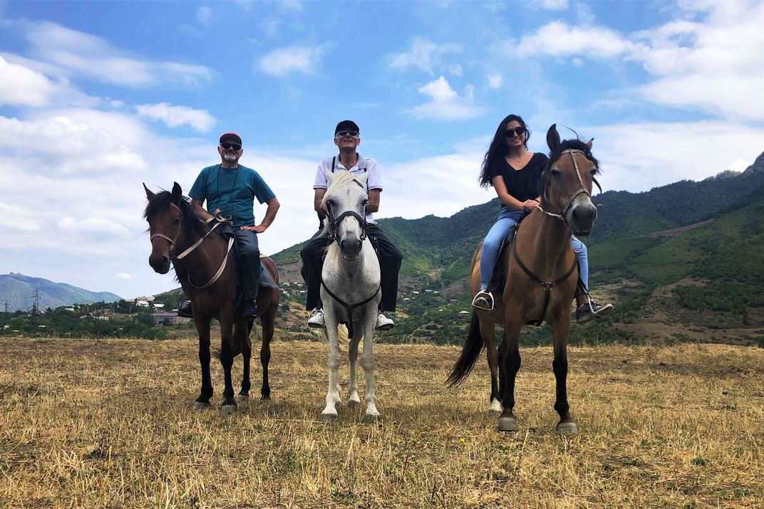 Three smiling people sit on horseback neck to each other. 