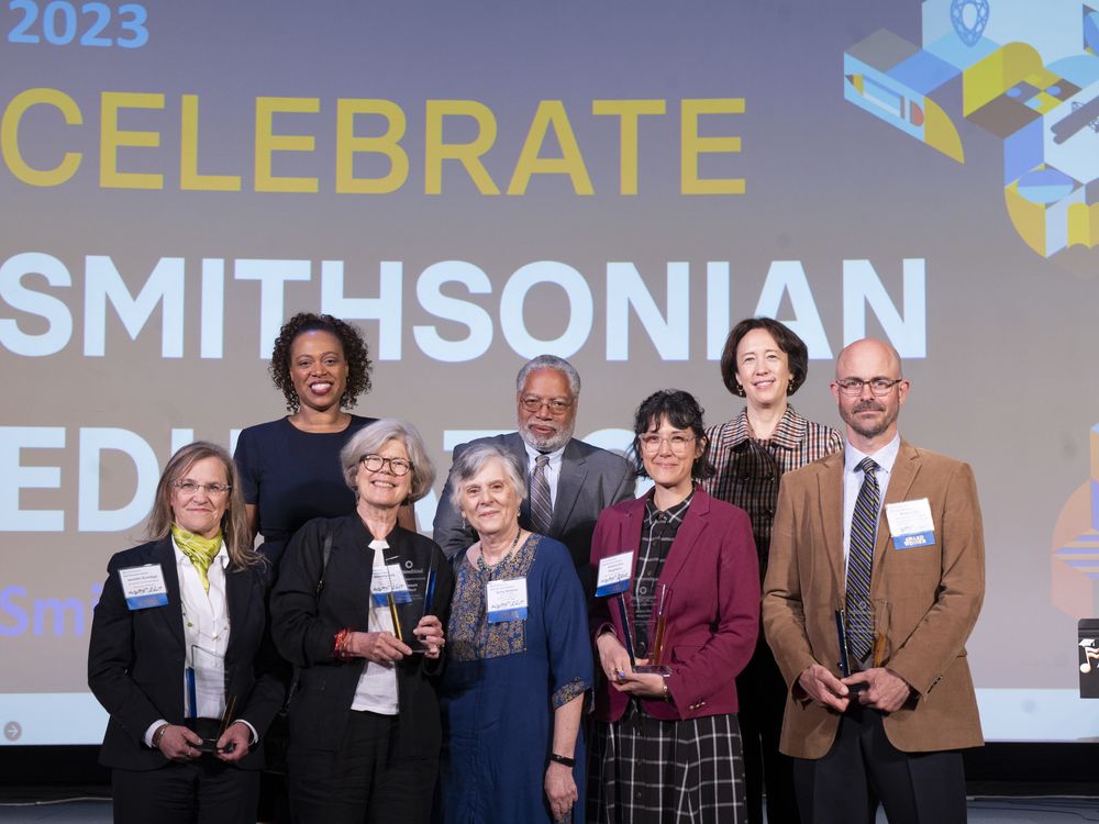Group of Smithsonian Education awardees with leadership standing in front of a large screen that says "Celebrate Smithsonian Education"