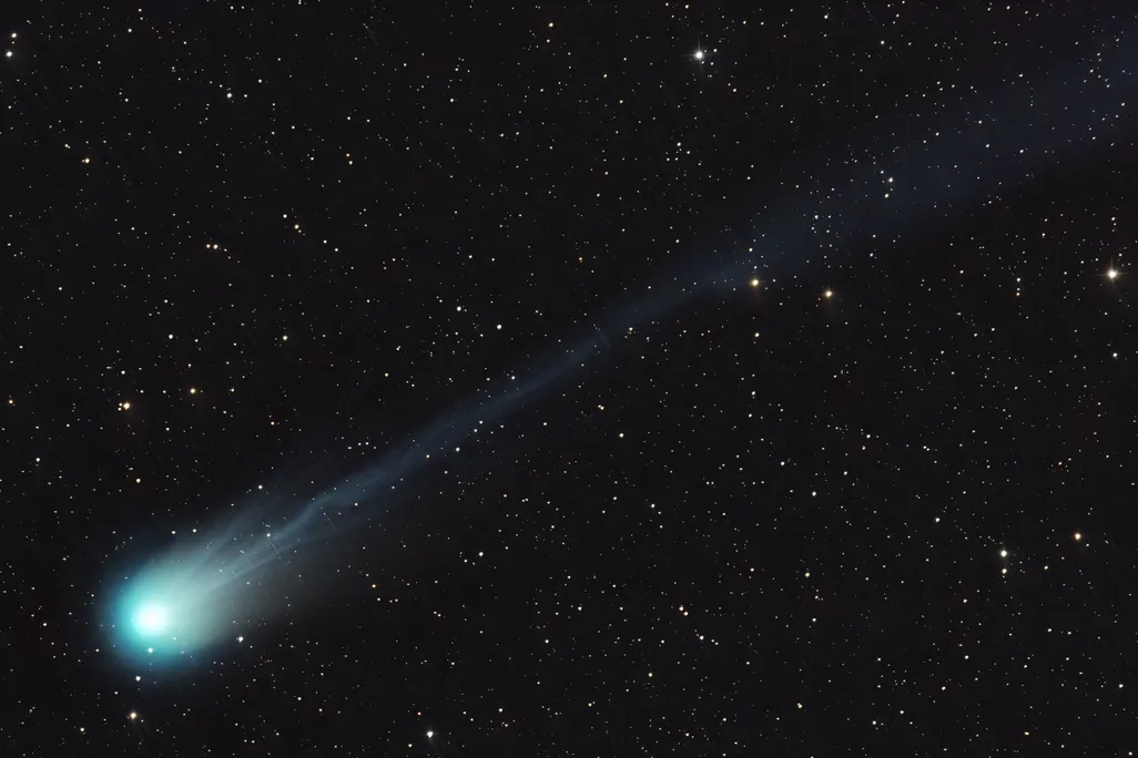 a comet streaks diagonally across the frame, with its bright green nucleus at the bottom left