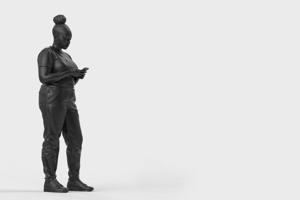 A bronze statue of a black woman surrounded by a plain white background. The woman is standing casually and looking down at her mobile phone, which she holds with both hands.