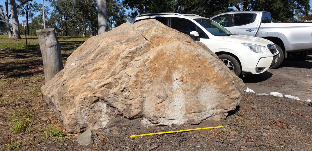 Large boulder with a footprint on it and cars behind it