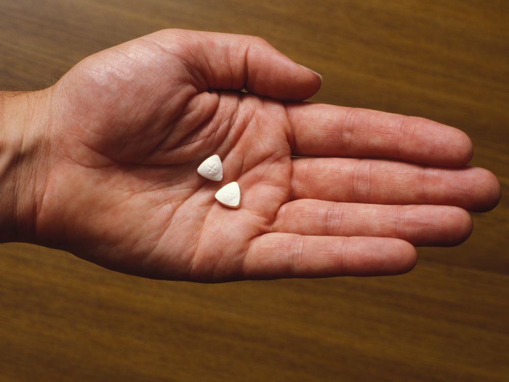 A person's open hand holding two triangle-shaped pills