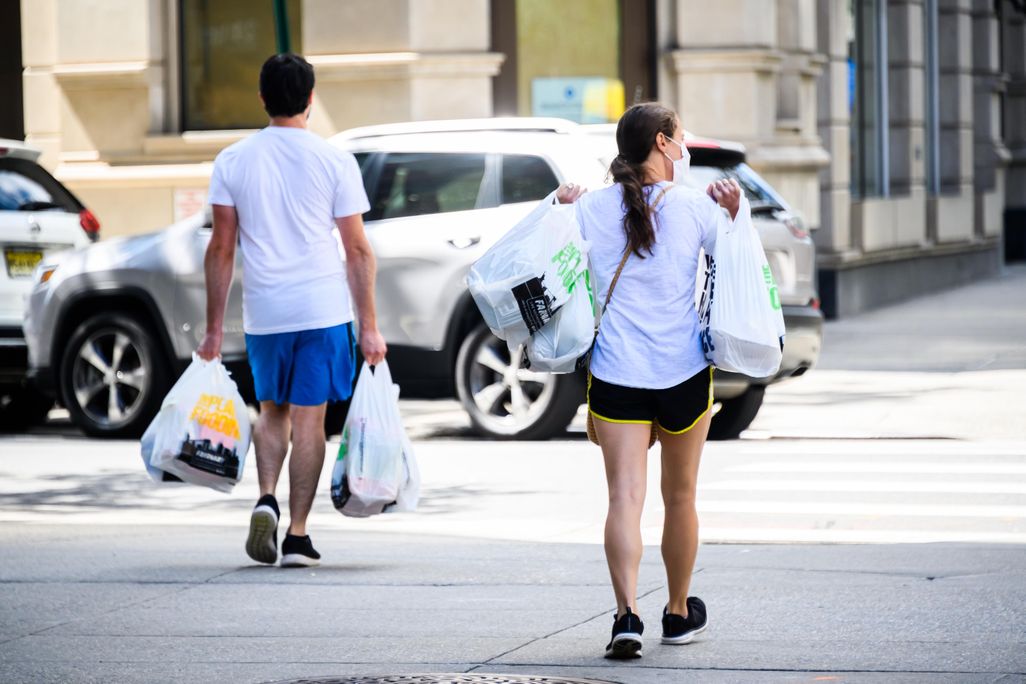 Two people walk down street carrying groceries in plastic bags in New York