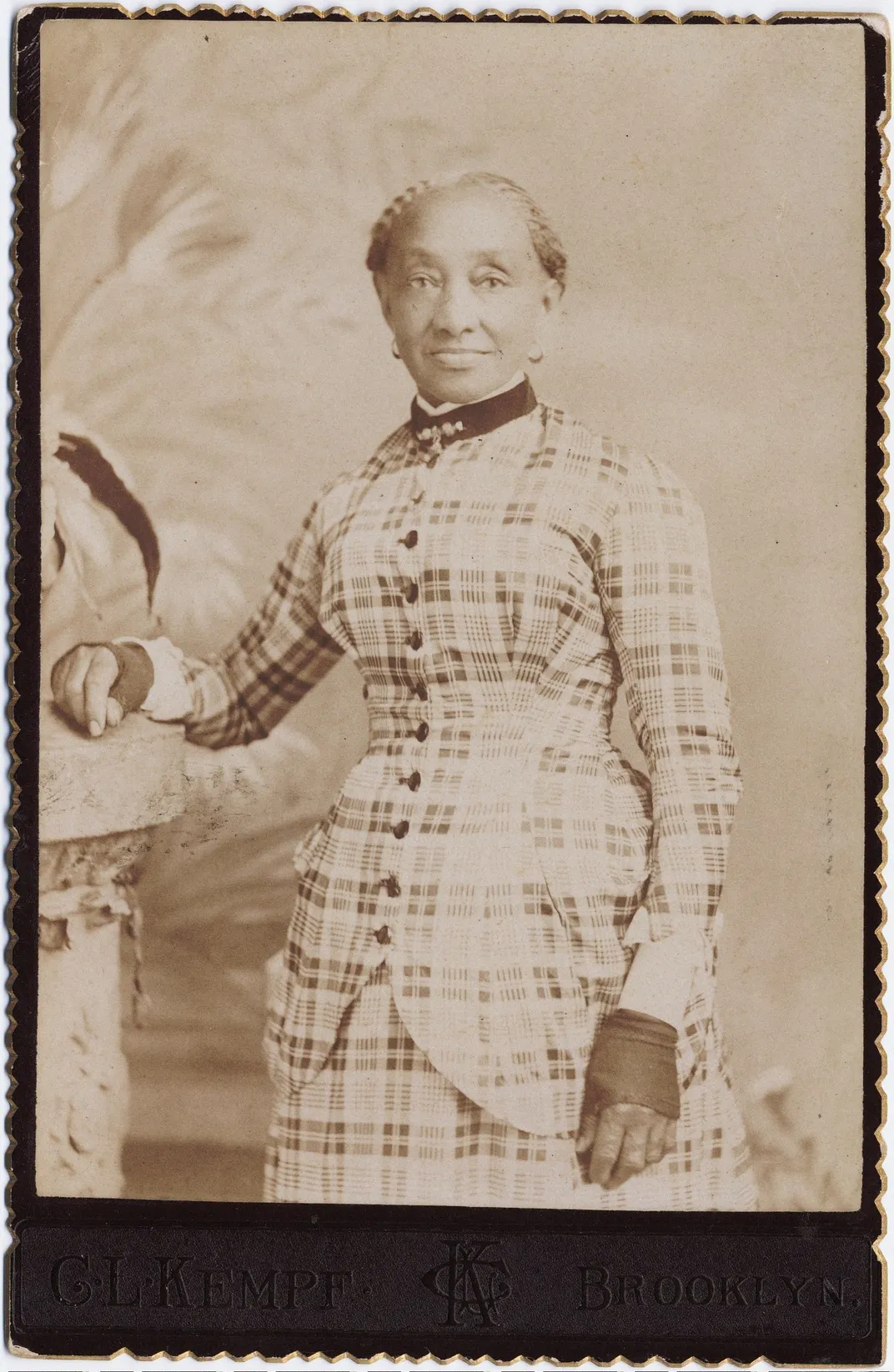 Three-quarter length portrait of an elderly lady in a plaid dress, circa 1890