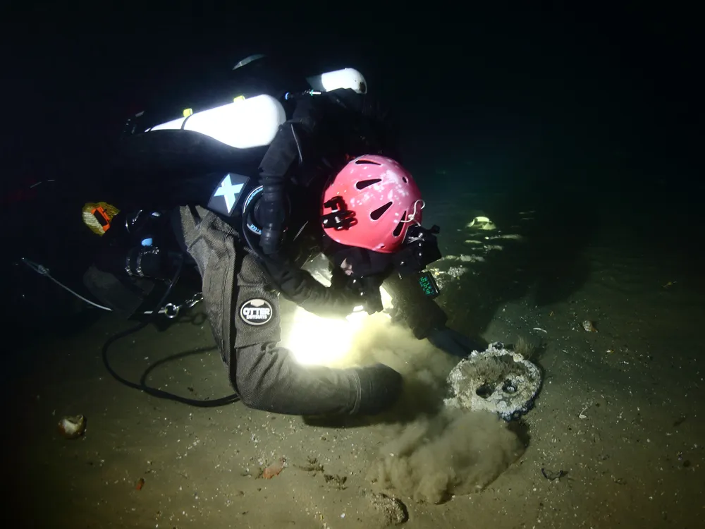 Underwater diver wearing a helmet shining a light on bottom of ocean floor