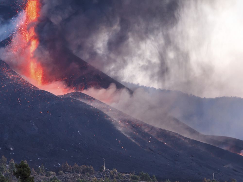 An image of the La Palma volcano erupting. A fountain of lava is seen spewing from the mountain.