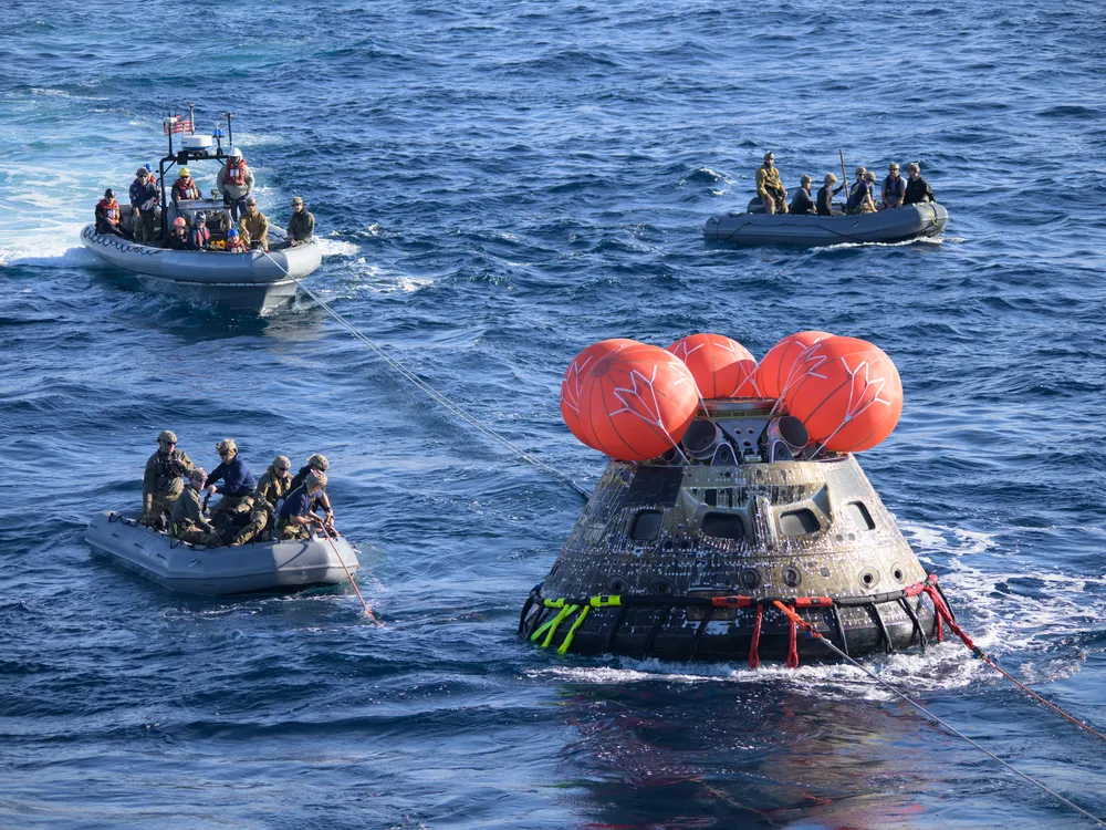 Three boats tug the Orion spacecraft in the ocean