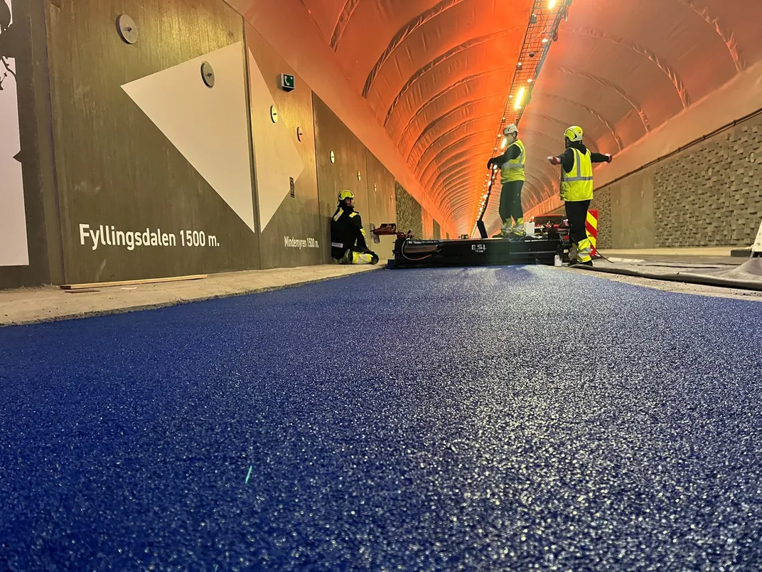 Crews in neon green safety gear installing blue rubber inside tunnel