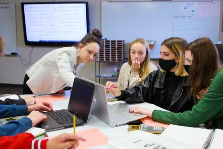 Peterson wears a bun and blazer pointing towards a computer screen with her students