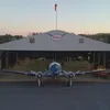 A propellor plane is in front of an open hangar